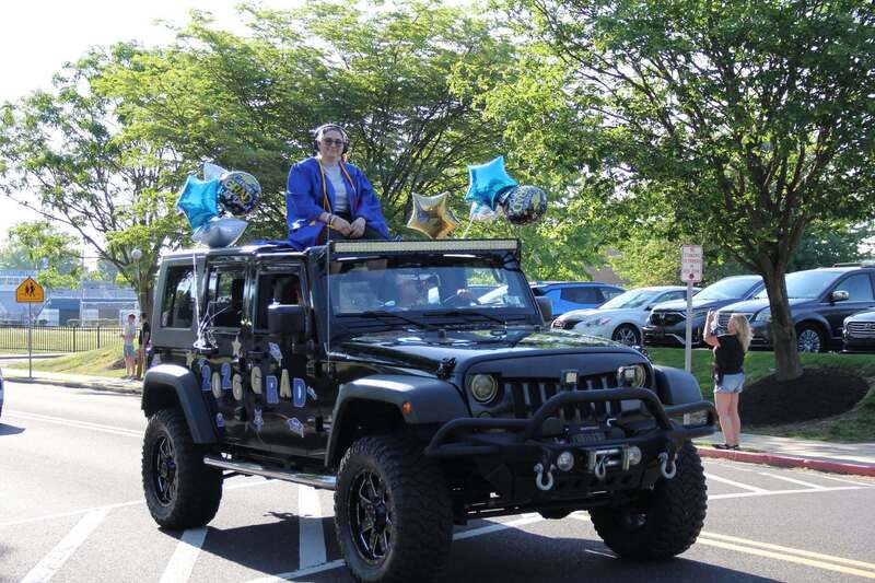 1 Student waves from the sun roof of a decorate black jeep
