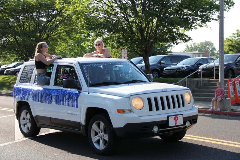 Students wave from the windows of a white jeep