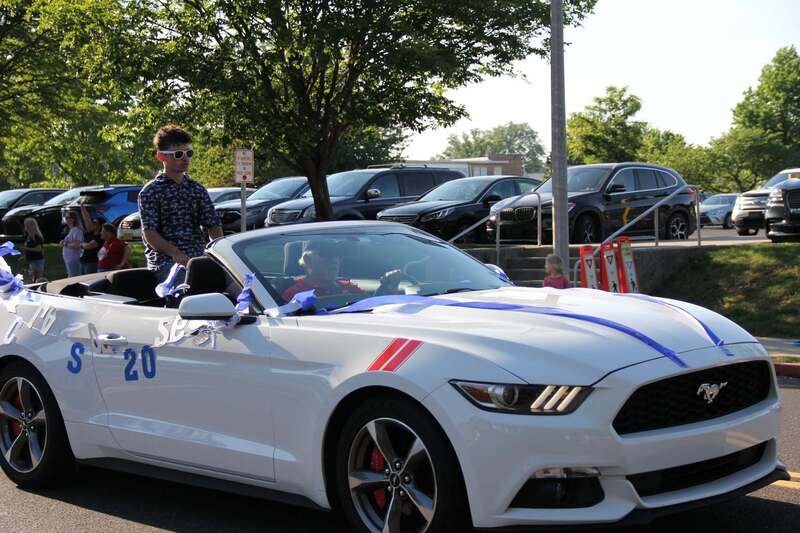 Students wave as they sit in the back of a white convertible mustang