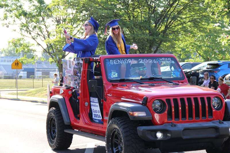 Students spray confetti onto the crowd from a red jeep