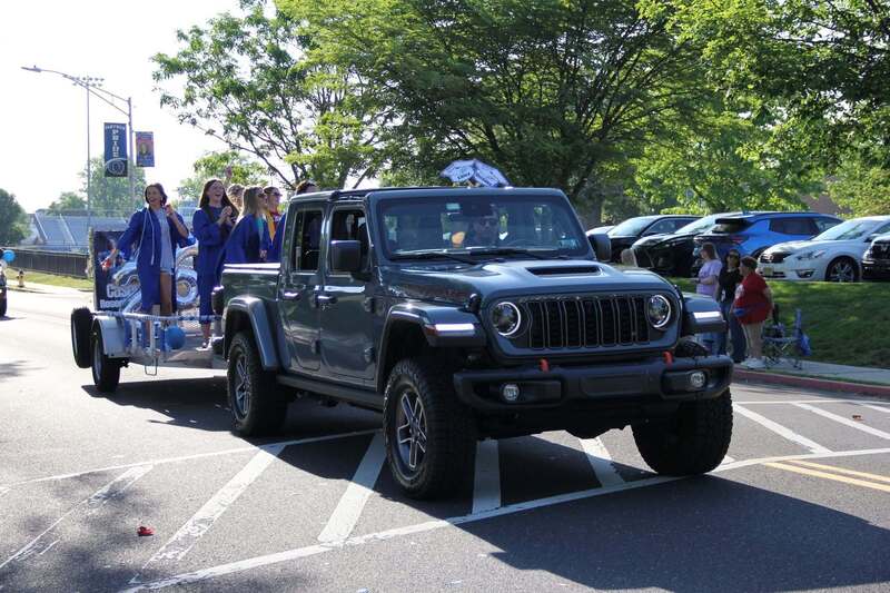 Students wave from a trailer being pulled a pick up truck