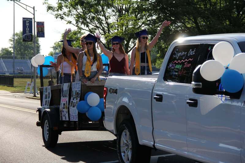 Students stand in a trailor being pulled by a white pick up truck