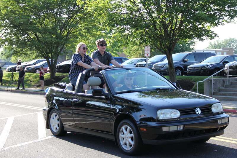 Students stand in the back of a volkswagon convertible and wave to the crowd