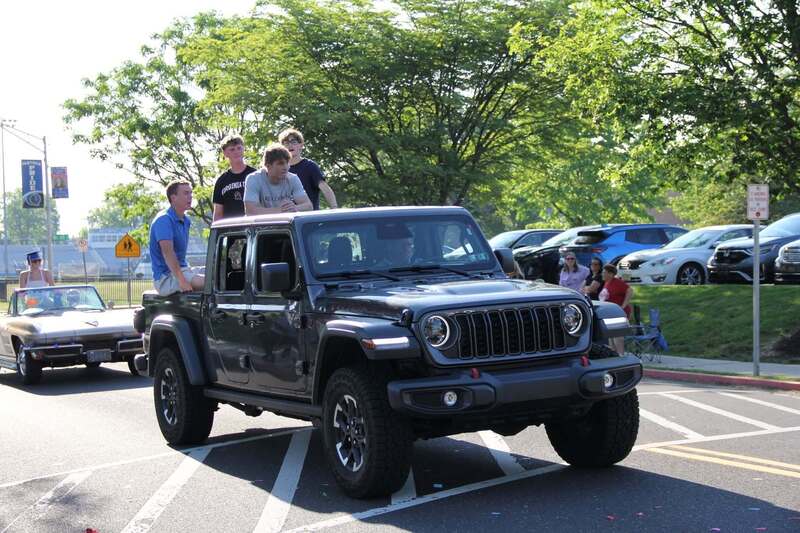 Students stand in the back of a Jeep truck to wave to the crowd