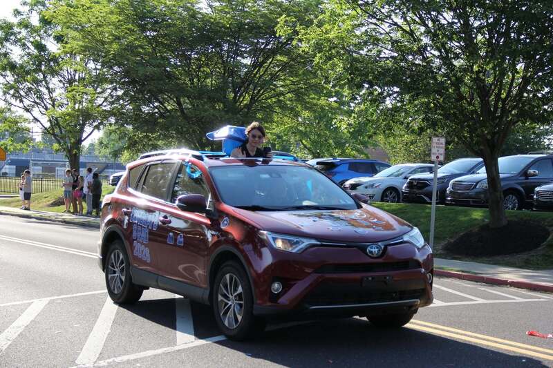 Students stands through car's sun roof to wave to the crowd