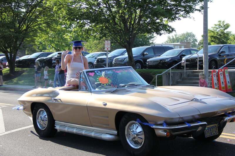 Student sits in the back of a convertible and waves to the crow