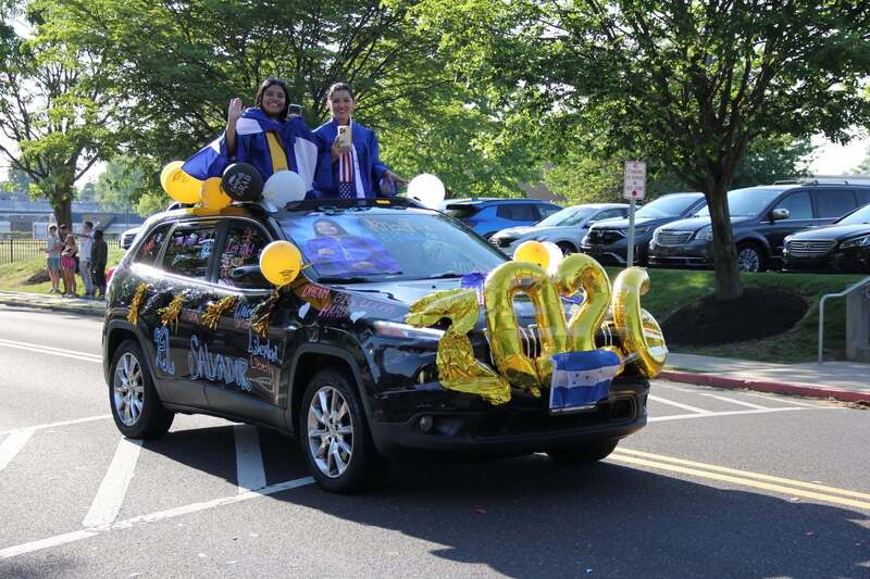 Two students stand out of their decorated car's sun roof to wave to the crowd