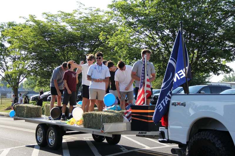 Students cheer from a trailor being pulled by a white pick up
