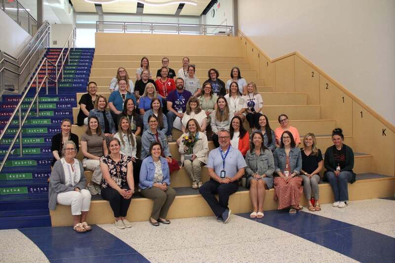 The entire staff smiles with Mrs. Demchick on the learning steps