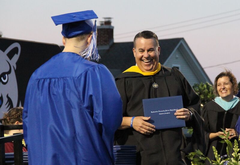 Principal Juan Soto smiles as he hands a diploma to a graduate