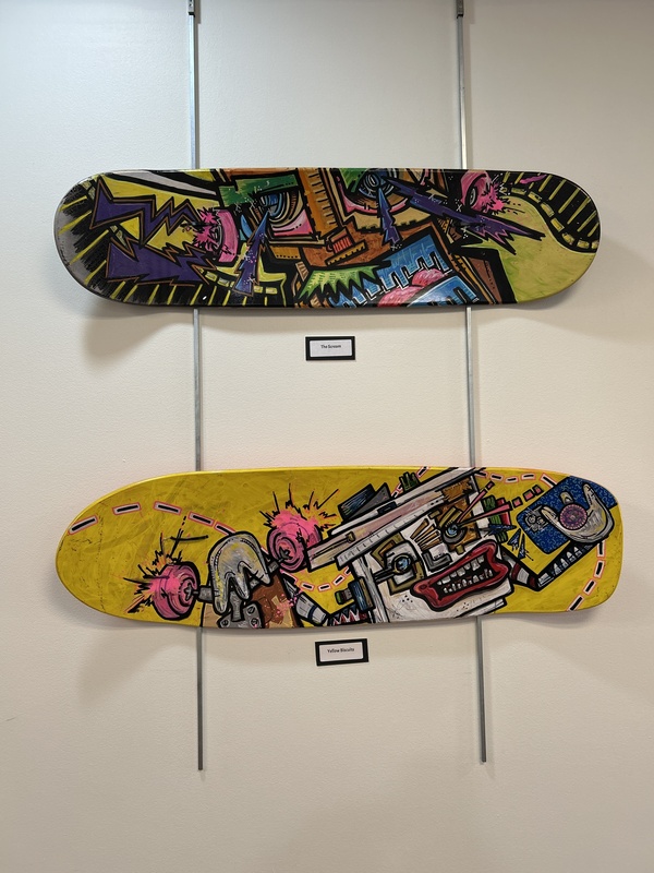 A photo of skateboard decks that are painted with images of radios, guitars and other lifestyle objects