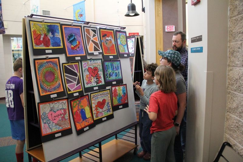 Students point out their artwork to their family.