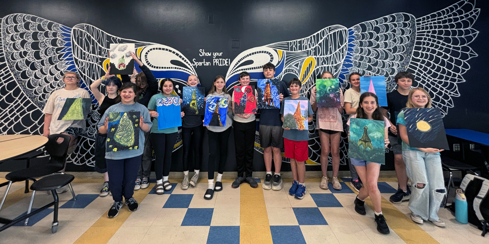 Students stand in QMS cafeteria with paintings.