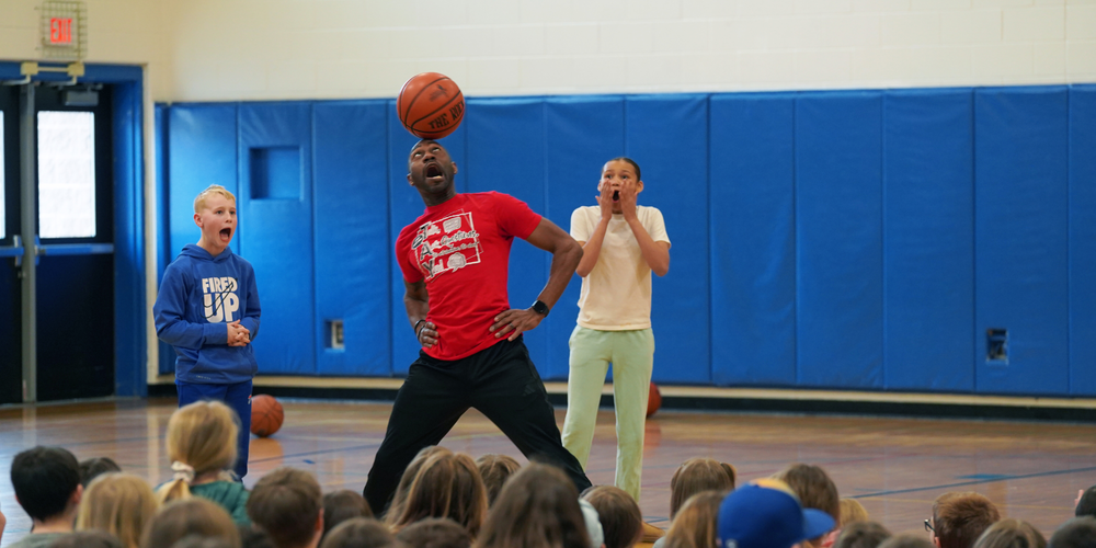 Tay Fisher spins a basketball on his head while shocked students watch.
