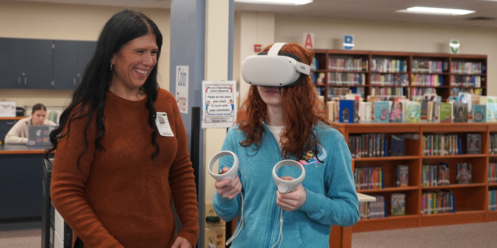 Kayla Sherman helps a student navigate a virtual reality headset.