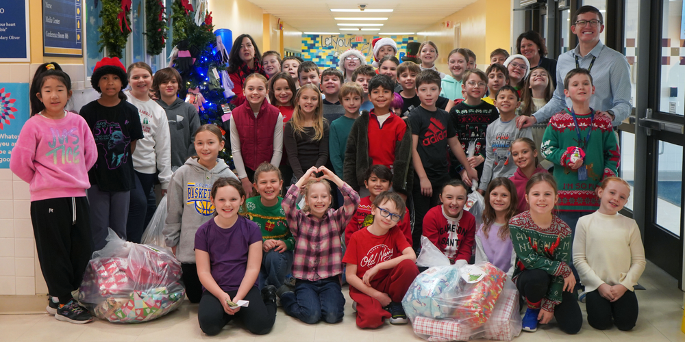Students pose in school hallway with bags of Christmas gifts to donate.