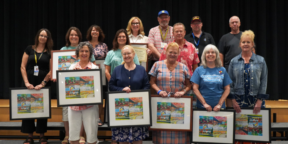 Retirees stand in group holding framed pictures.
