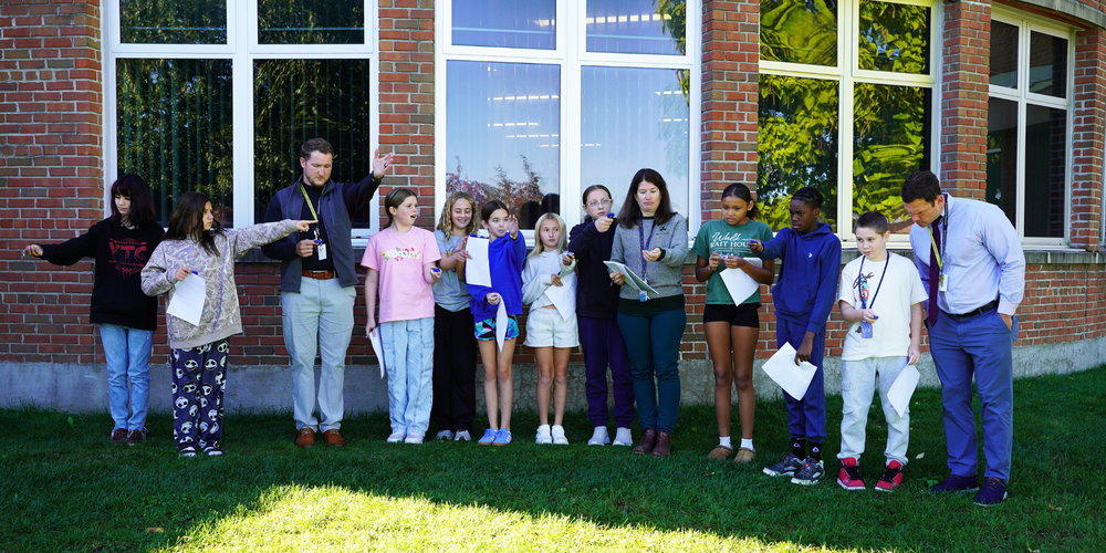 Students and teachers try land surveying holding compasses out behind Queensbury Middle School.