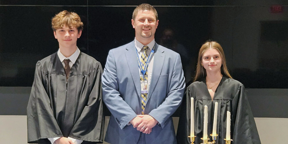 Two students stand with principal at NHS induction ceremony.