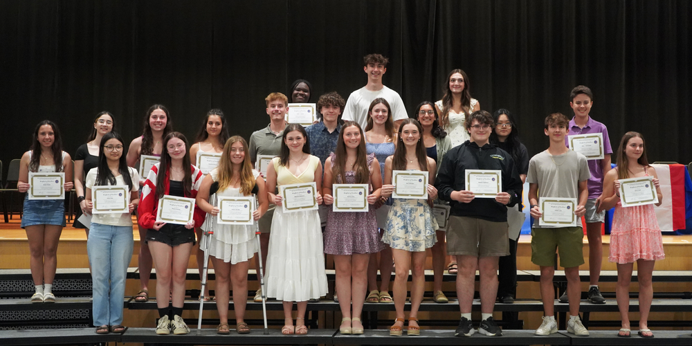 Students stand with certificates on risers.