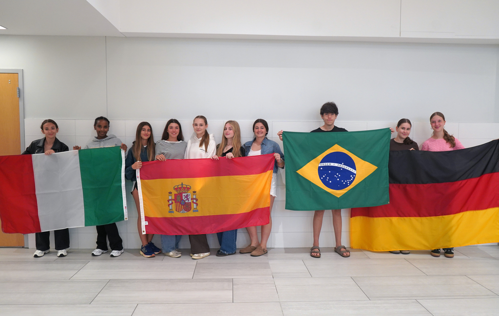 Students from four countries stand in QHS lobby with their flags.