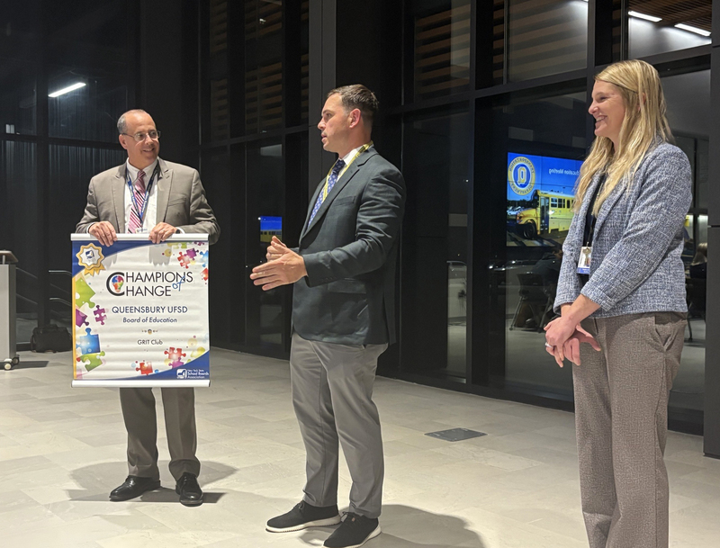 Superintedent of Schools Kyle Gannon holds Champions of Change banner along with QMS Principal Nick McPartland and GRIT club advisor Sam Gailor.