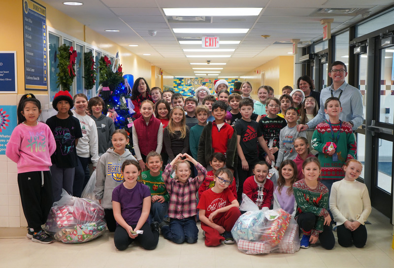 Students pose in school hallway with bags of gifts to donate.
