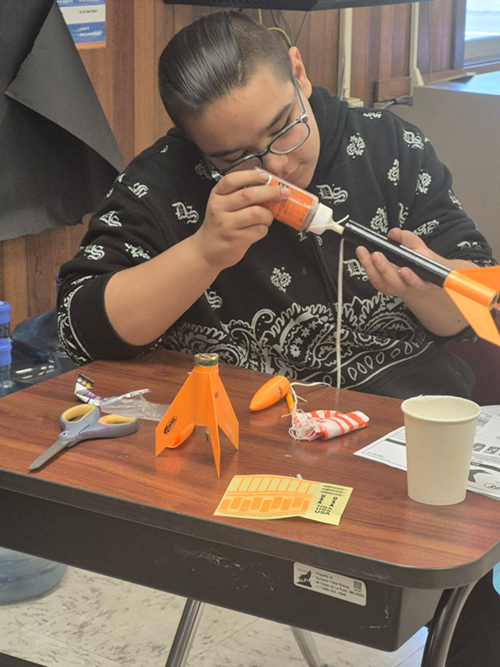 Student building a rocket and adding a piece with glues. 