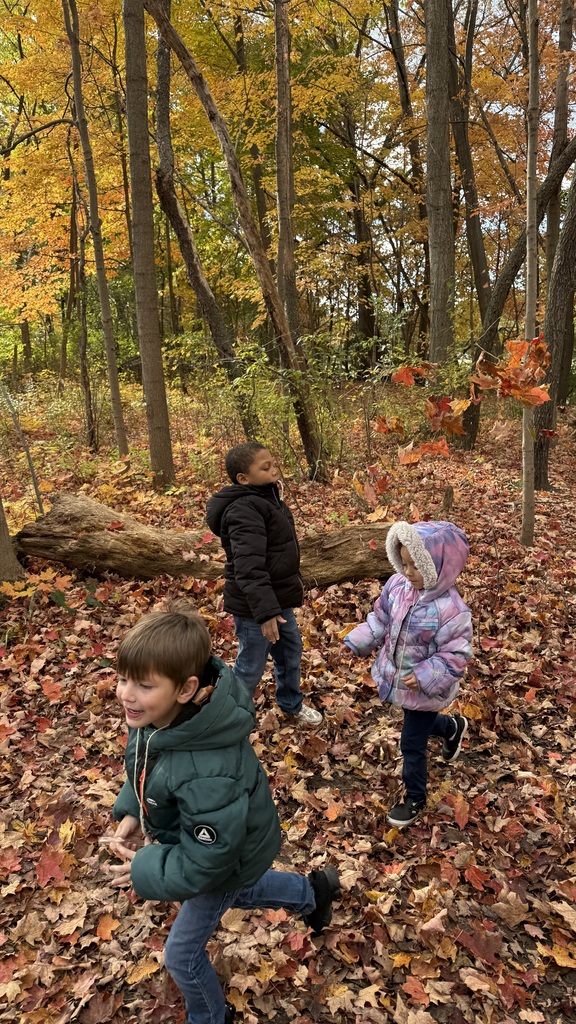 Three students run through the orange and brown leaves at Riverbend Nature Center 