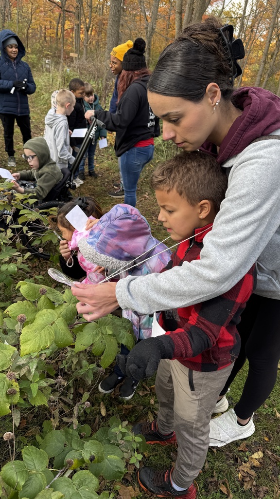 A student and a chaperone using a magnifying glass to view plants.