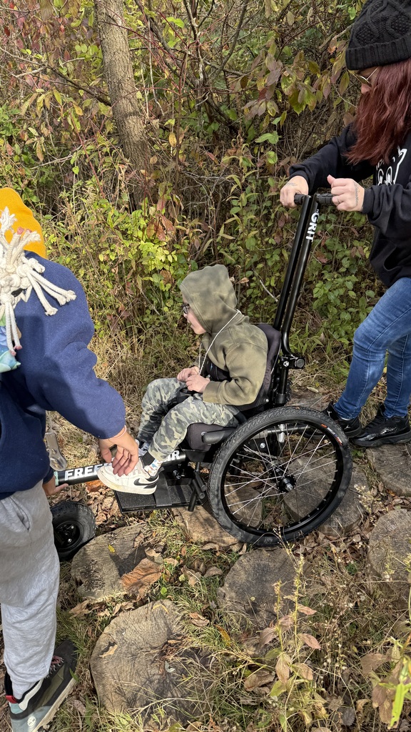 Angel Martz and his mother traversing a log pathway in a GRIT Freedom Chair.