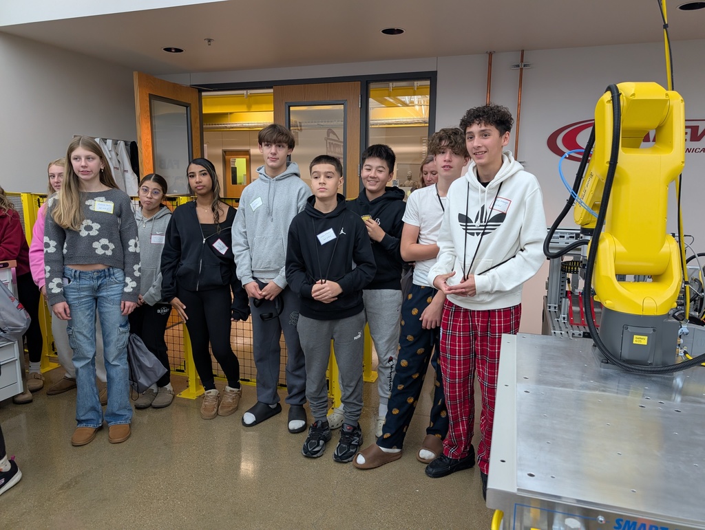 A group of students listening to an instructor talk about robotics.