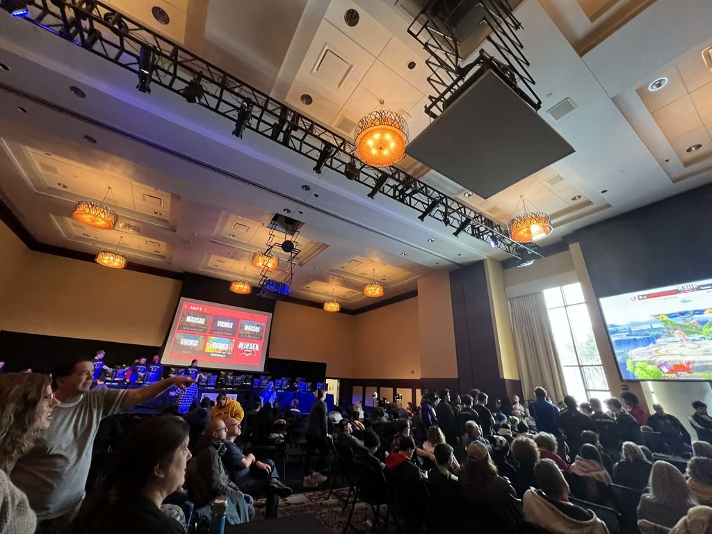 A wide shot of the competition hall. Several players spectate as others compete.