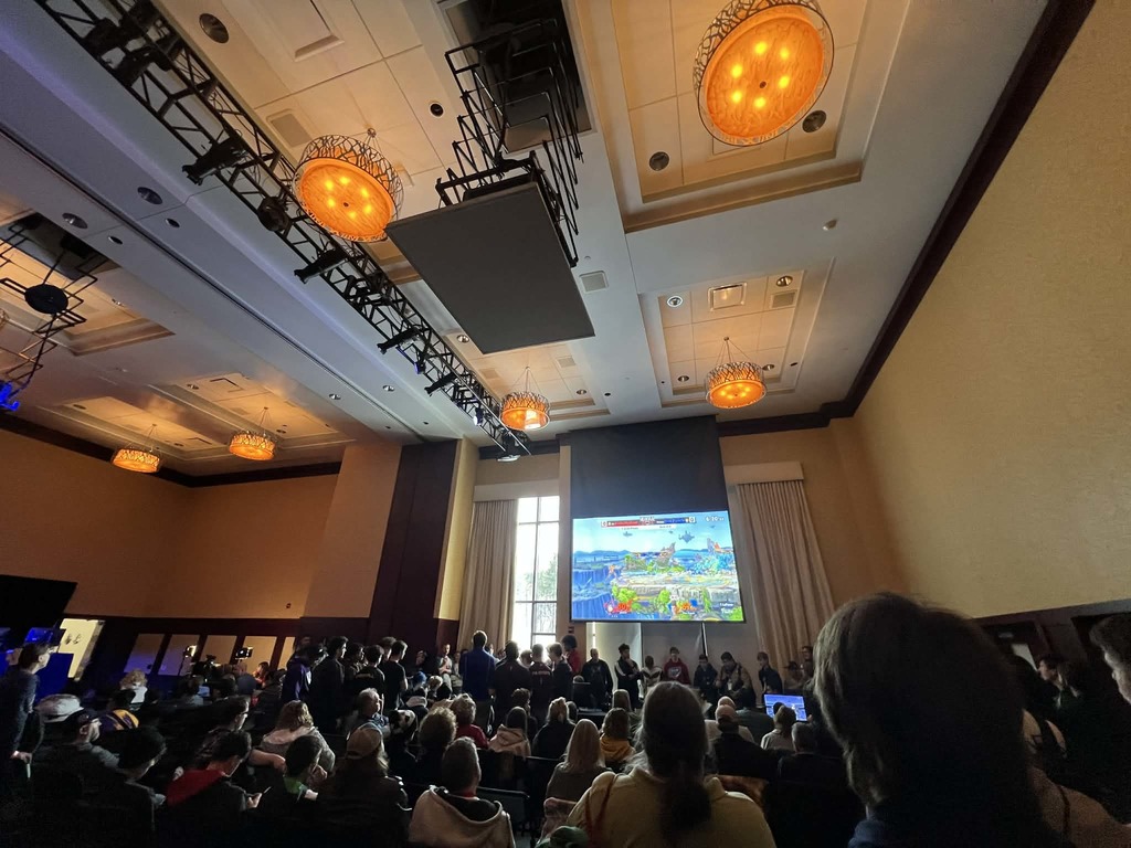 A wide shot of the competition hall. Several players spectate as others compete.