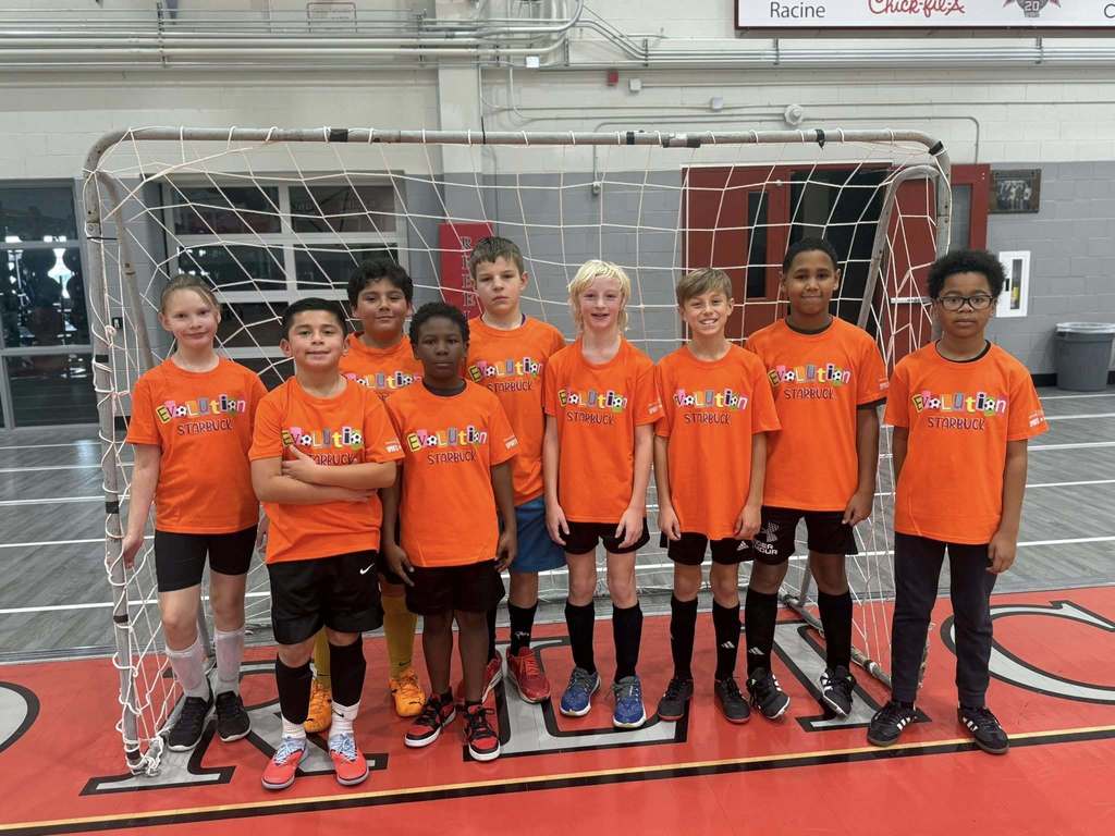 Nine students, wearing their Evolution soccer league shirts, standing in front of a soccer goal.