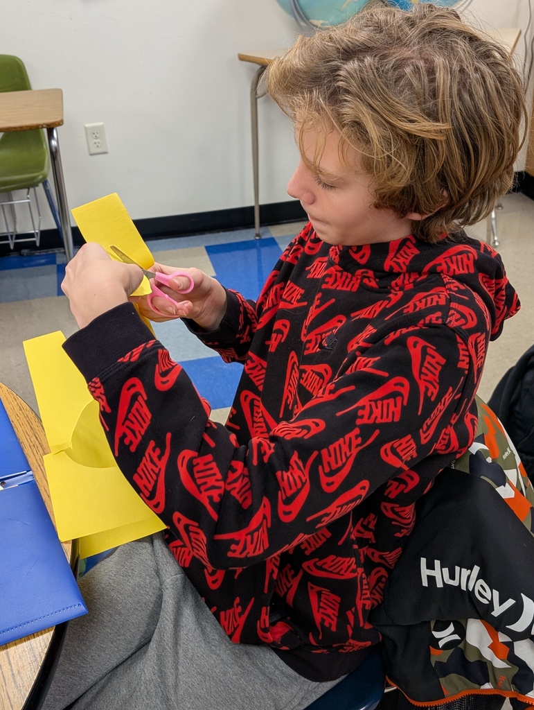 A male student cuts a sheet of yellow construction paper.