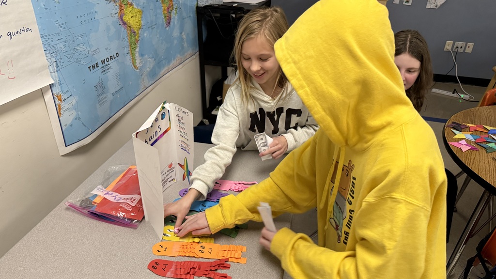 A female student sells a yellow paper jellyfish she made to a male student.