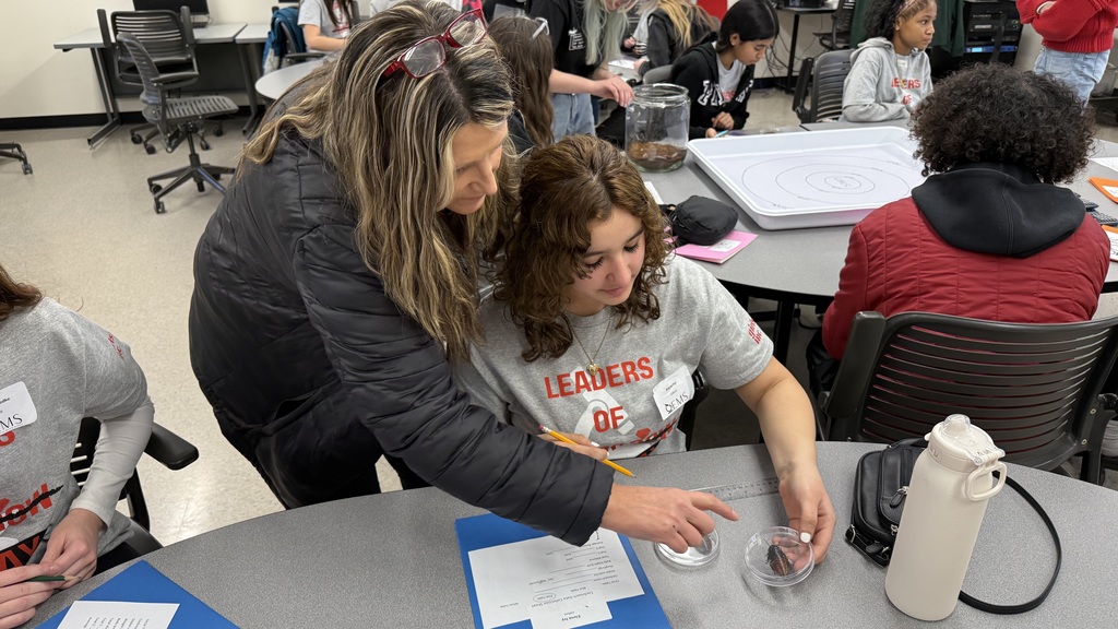 A teacher helps a student measure a cockroach in a lap experiment.