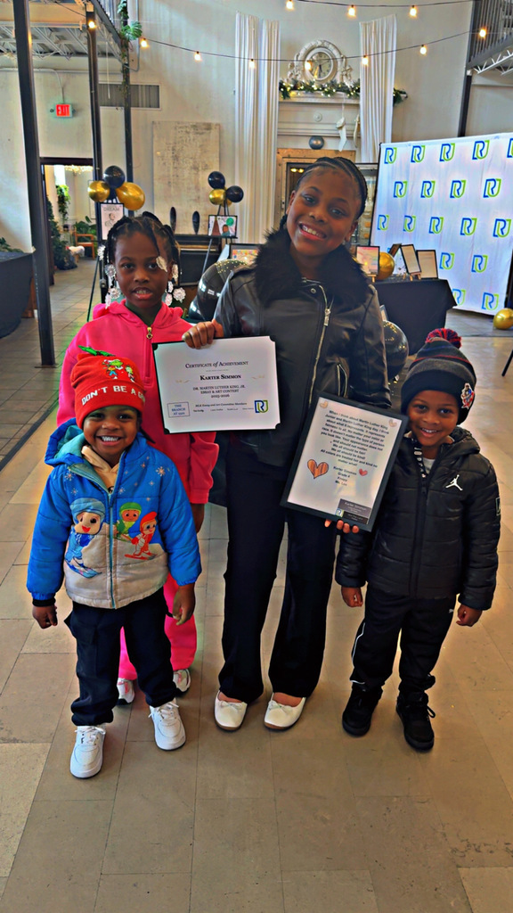 A student posing for a photo with her award, with her siblings.