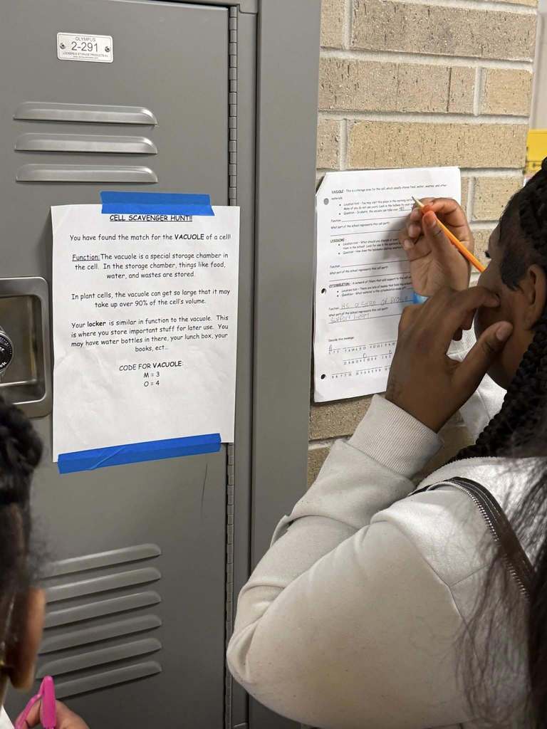 A scavenger hunt clue is posted on a locker and students are working on their assignment.
