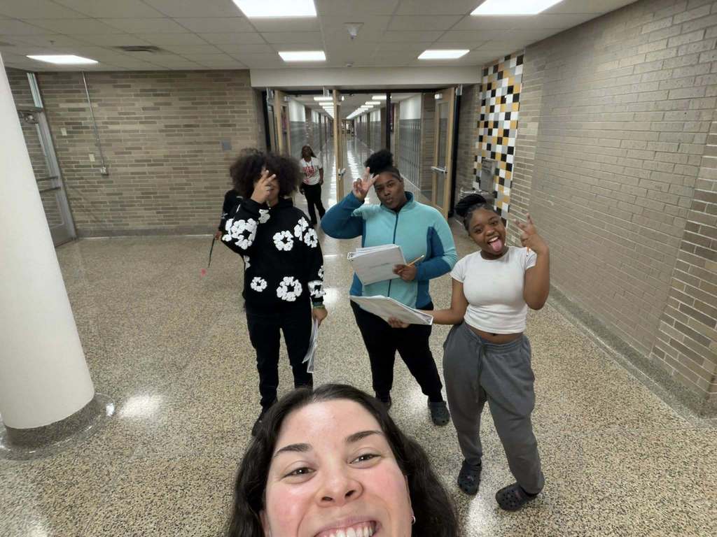 Ms. Weisbrod poses for a picture with three of her students in the hallway.