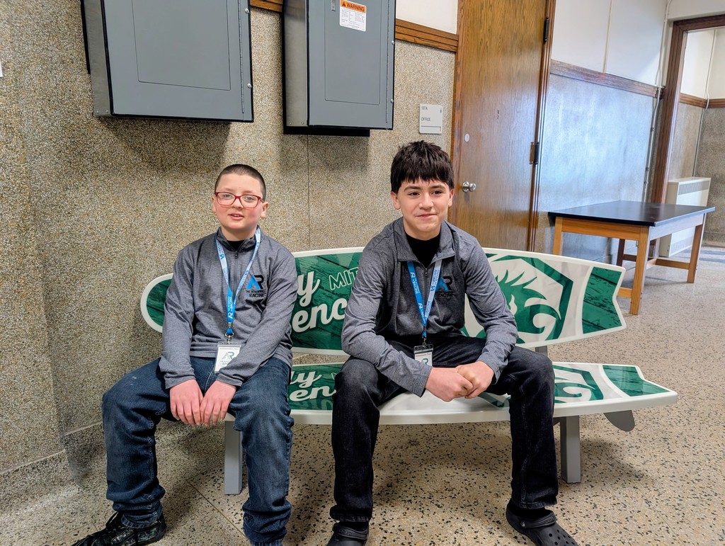 Two middle school boys in student ambassador uniforms and blue Academy lanyards sit on the bench.