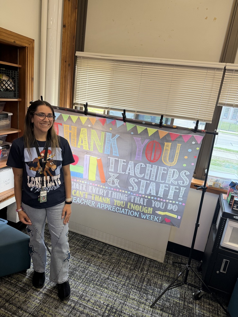 A teacher standing beside a sign that says "Thank you teachers & staff. We appreciate everything that you do and can't thank you enough. Happy teacher appreciation week!"