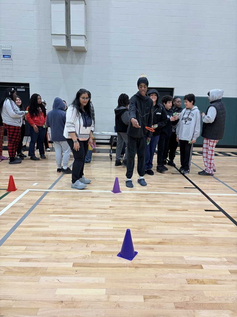 A male student playing a ring toss game while other students wait for their turn.