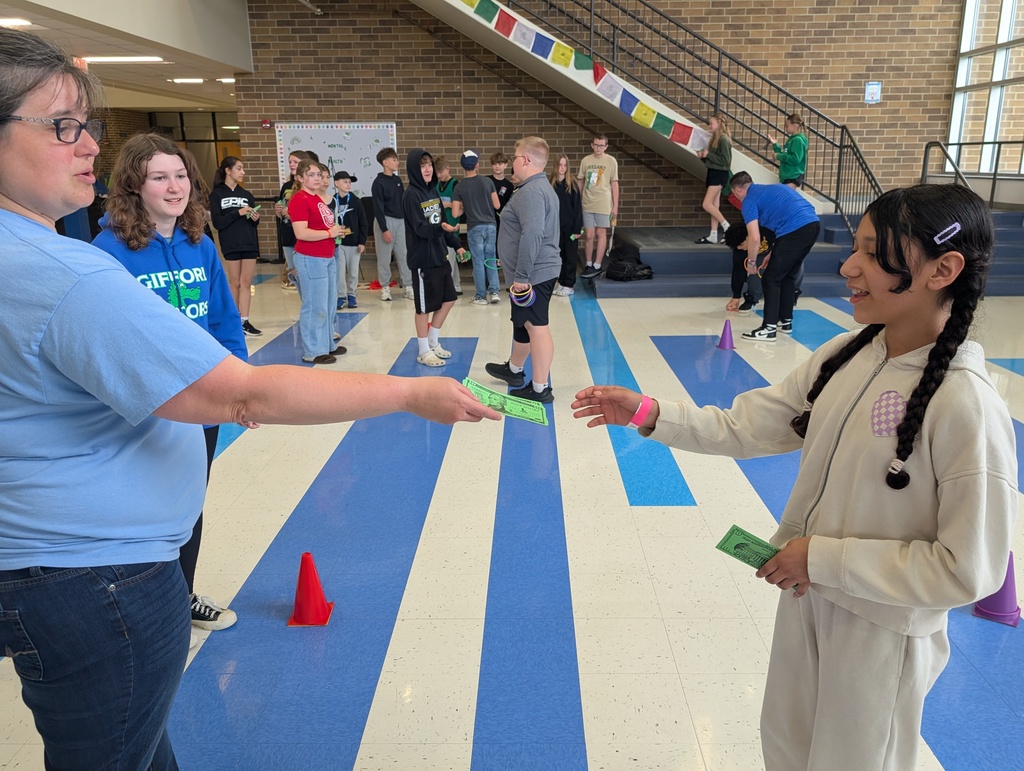A teacher handing fake money to a student who just completed a ring toss game.