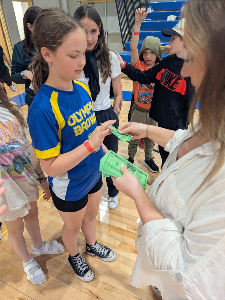 A teacher handing fake money to a student who just completed a ring toss game.