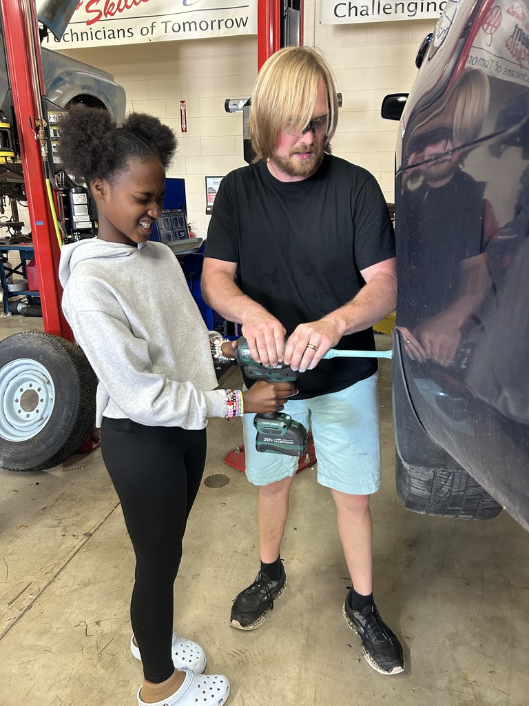 A Mitchell student tightens lugs nuts with a drill, with the assistance of Park's automotive instructor.