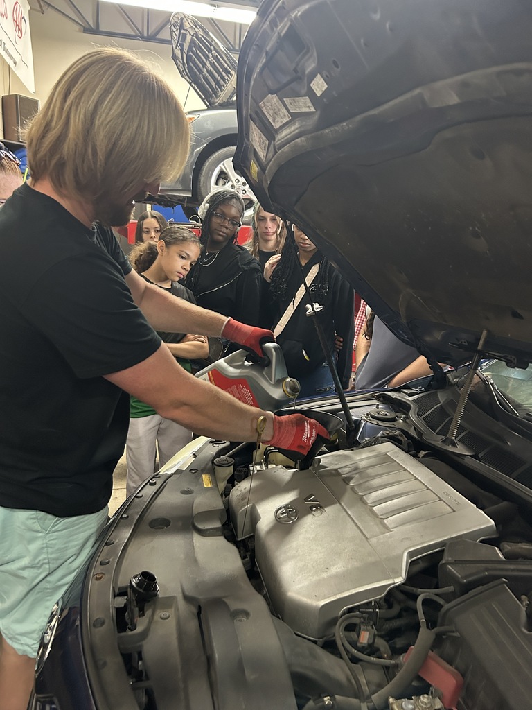 Park's automotive instructor points to a car's engine cover.