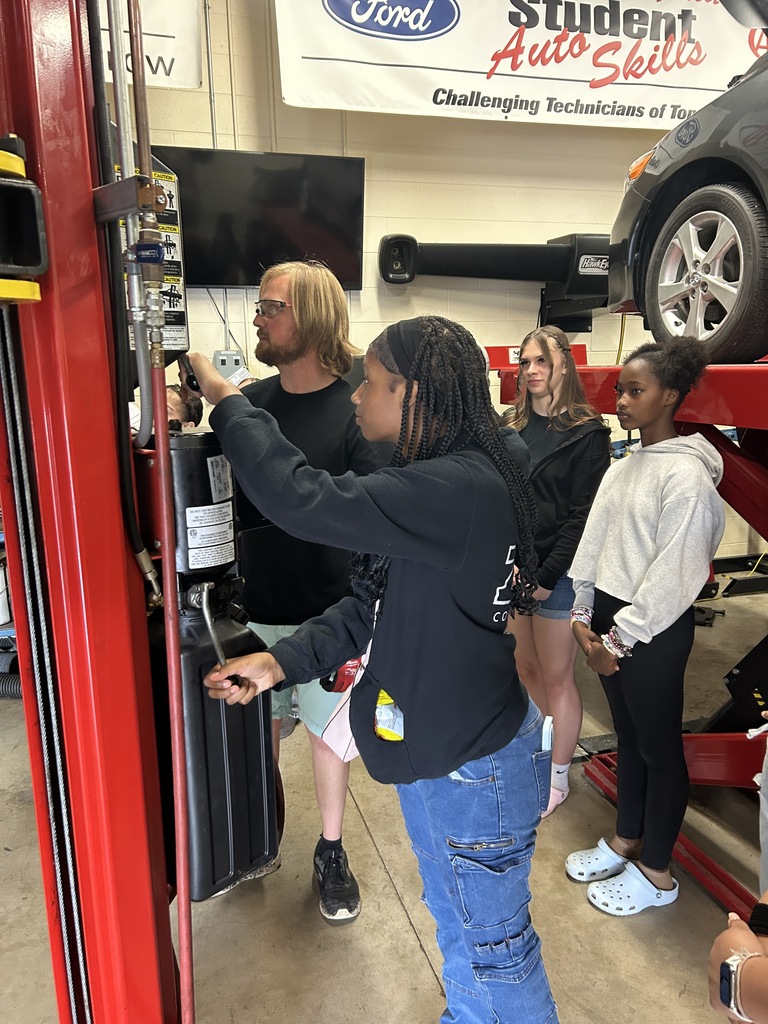 A student pulls a handle that lowers a vehicle on a lift.