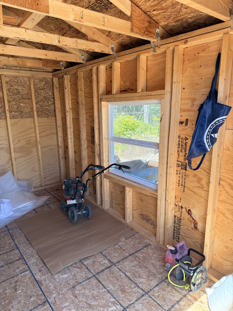 The inside of the storage shed. To the right is a tiller and a window.